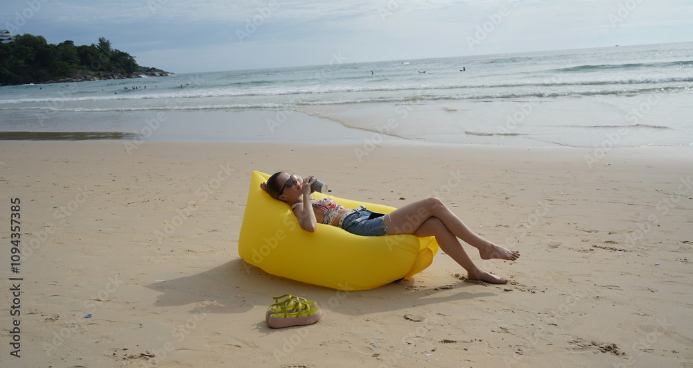 A young woman on the beach lounging on a yellow bean bag A young woman on the beach lounging on a yellow bean bag