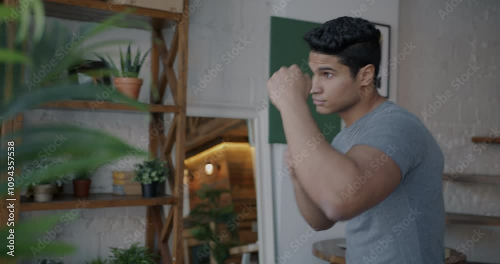 Confident Middle Eastern sportsman shadow fighting practicing boxing moves indoors in apartment. Sports and active lifestyle concept. Confident Middle Eastern sportsman shadow fighting practicing boxing moves indoors in apartment. Sports and active lifestyle concept.