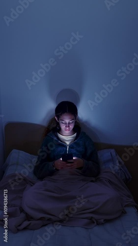4K teenager girl using a smartphone lying in bed late at night, playing games, watching videos, and typing. Children's screen addiction. Screen Addiction in Youth