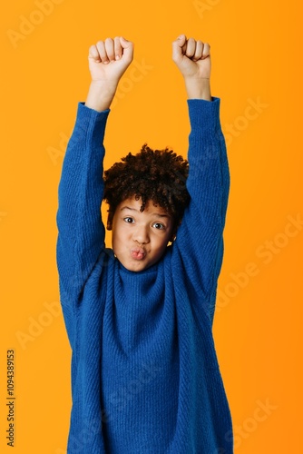 Triumphant young african american boy celebrating victory with raised hands against a vibrant orange background photo