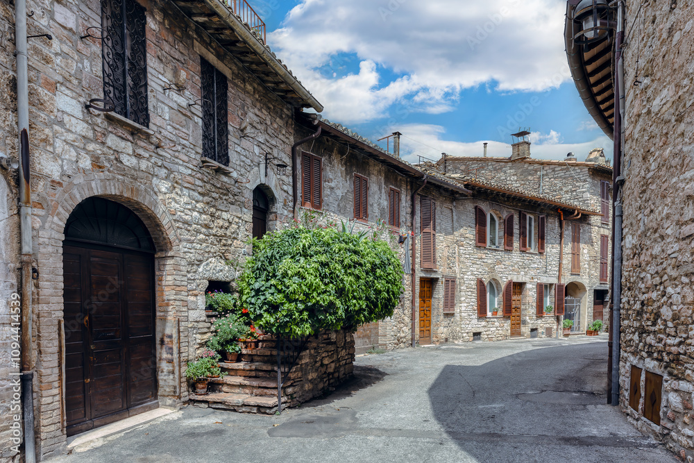 A charming cobblestone street in medieval Assisi, (Umbria, Italy), featuring ancient stone buildings and vibrant flower pots