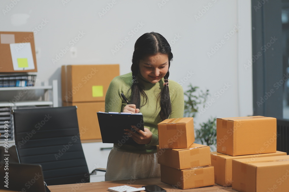 Startup SME small business entrepreneur of freelance Asian woman wearing apron using laptop and box to receive and review orders online to prepare to pack sell to customers, online sme business ideas. Startup SME small business entrepreneur of freelance Asian woman wearing apron using laptop and box to receive and review orders online to prepare to pack sell to customers, online sme business ideas.