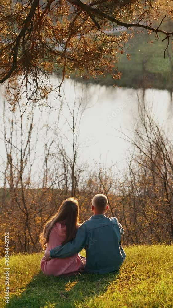 Couple in love resting among autumn nature. Young man and woman sitting on the hill and admiring the river at sunset. Vertical video Couple in love resting among autumn nature. Young man and woman sitting on the hill and admiring the river at sunset. Vertical video