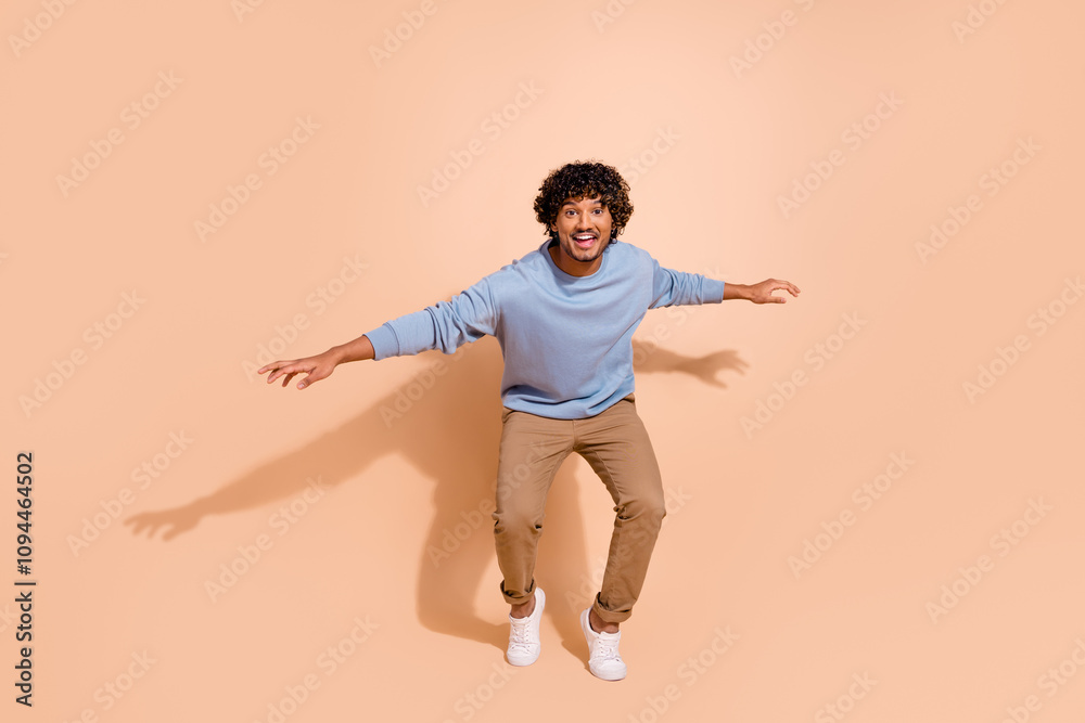 Full body photo of good mood eccentric guy wear blue shirt trousers standing on tiptoes having fun isolated on beige color background Full body photo of good mood eccentric guy wear blue shirt trousers standing on tiptoes having fun isolated on beige color background