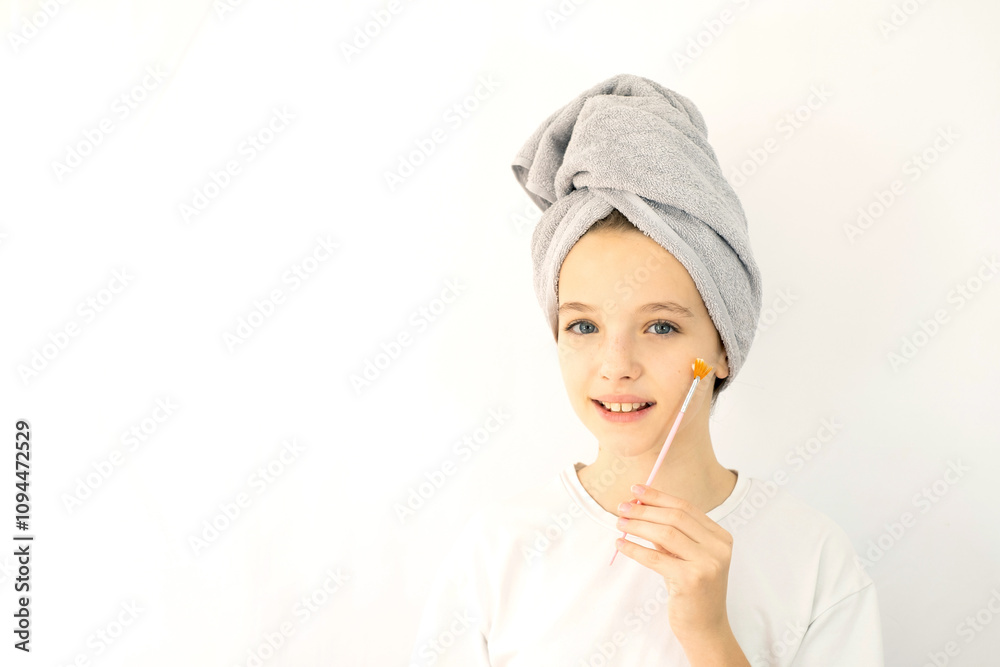 Beautiful teenage girl with towel on her head smiling and taking care of her facial skin with a brush. Skin care for a teenager. White background, space for text Beautiful teenage girl with towel on her head smiling and taking care of her facial skin with a brush. Skin care for a teenager. White background, space for text