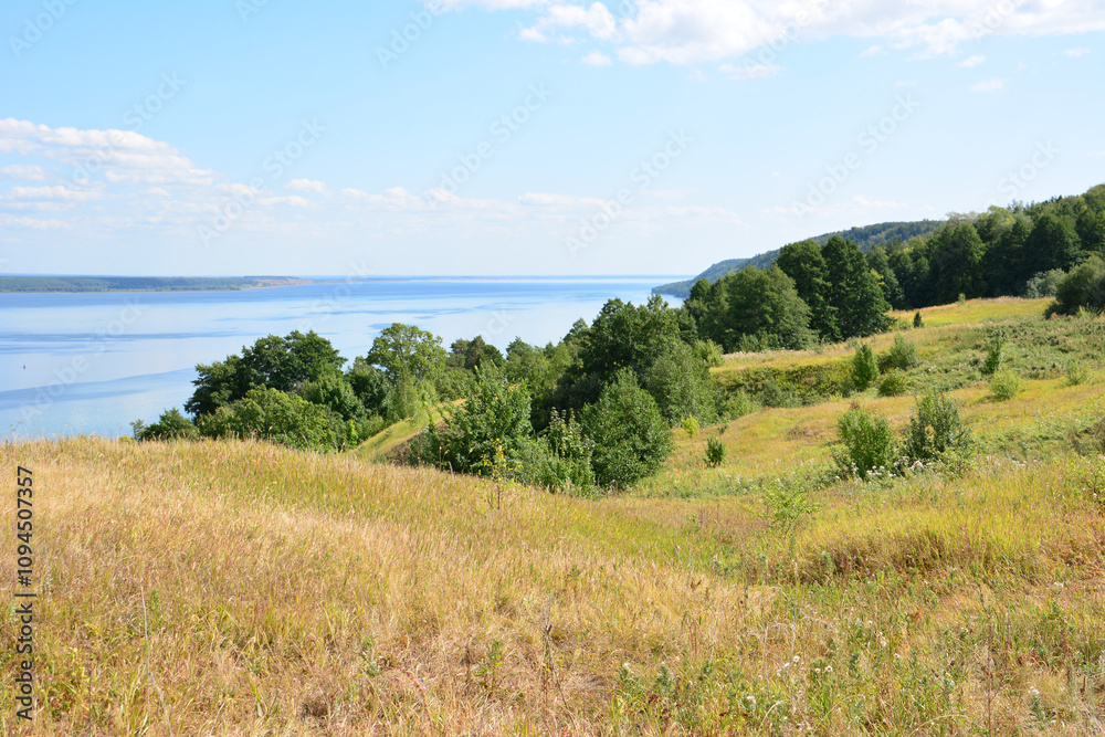 a hill with a lake and trees on the horizon and blue river and sky a hill with a lake and trees on the horizon and blue river and sky