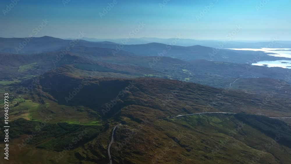 Caha Pass, County Cork, Ireland, September 2024. Drone tracks right in a panoramic high angle overview of a winding road crossing the rugged mountain ridge and descending to the North Atlantic Ocean. Caha Pass, County Cork, Ireland, September 2024. Drone tracks right in a panoramic high angle overview of a winding road crossing the rugged mountain ridge and descending to the North Atlantic Ocean.
