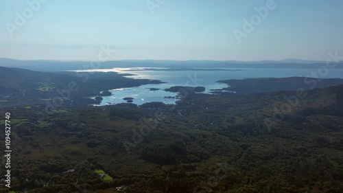 Caha Pass, County Cork, Ireland, September 2024. Drone tracks left over rolling forested hillside with the view south east to Glengarriff and the glistening North Atlantic Ocean in the distance. photo