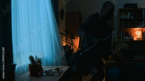Two criminals dressed in black clothes coming down from windowsill after breaking into property through window