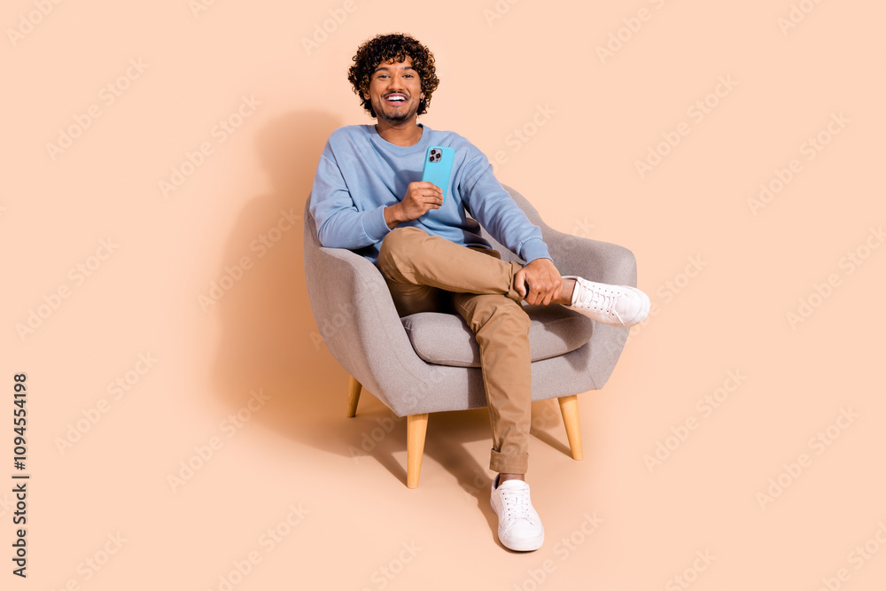 Full length photo of cute good mood guy dressed blue sweatshirt communicating modern device isolated beige color background Full length photo of cute good mood guy dressed blue sweatshirt communicating modern device isolated beige color background