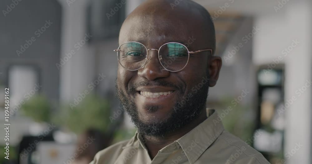 Close-up slow motion portrait of African American businessman looking at camera and smiling against blurred office background. Job and person concept.