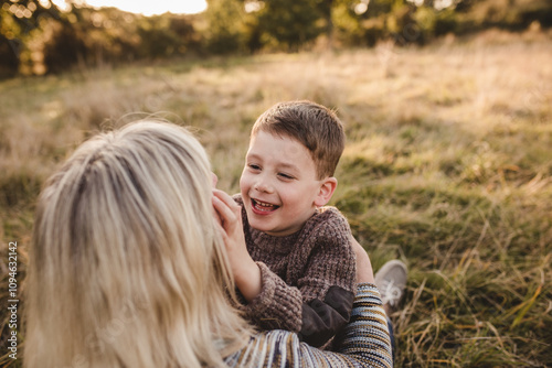 Smiling boy with mother outdoors in meadow, warm sunset light candid family portrait