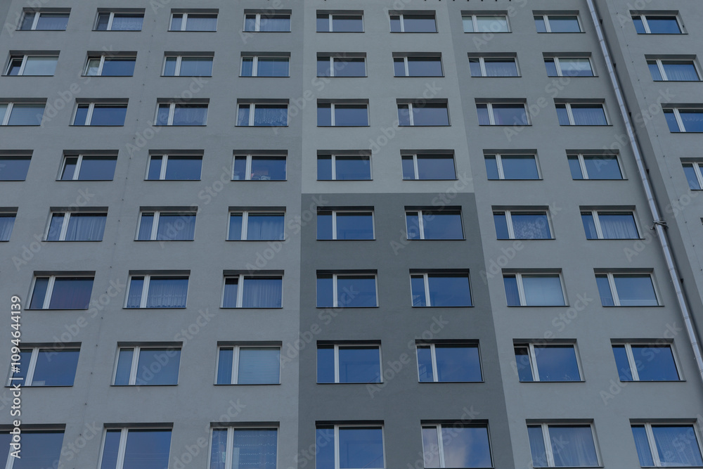 The facade of a highrise building showcases numerous rows of windows set against a muted gray background The facade of a highrise building showcases numerous rows of windows set against a muted gray background