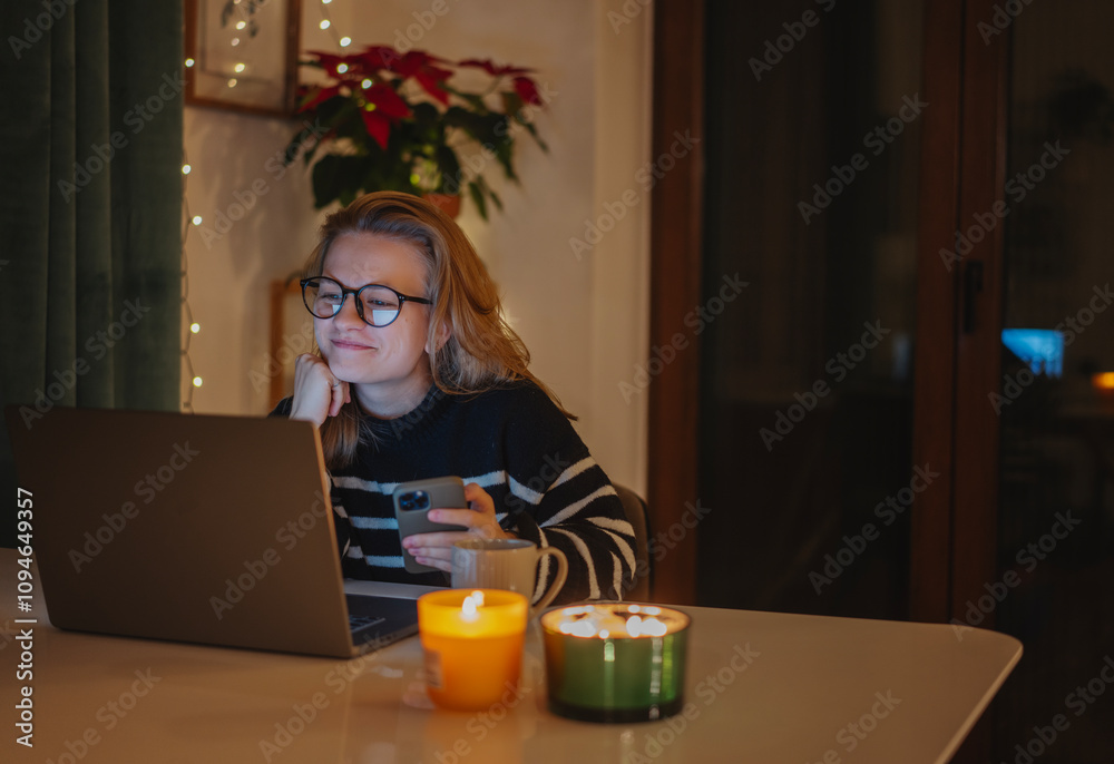 Young woman using laptop and smartphone while sitting at home during Christmas holidays. Cozy evening with candles Young woman using laptop and smartphone while sitting at home during Christmas holidays. Cozy evening with candles