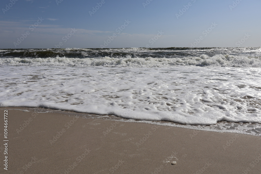 Ocean waves with white foam rolling onto a sandy beach under a clear blue sky, capturing the tranquility of the seaside. Ocean waves with white foam rolling onto a sandy beach under a clear blue sky, capturing the tranquility of the seaside.