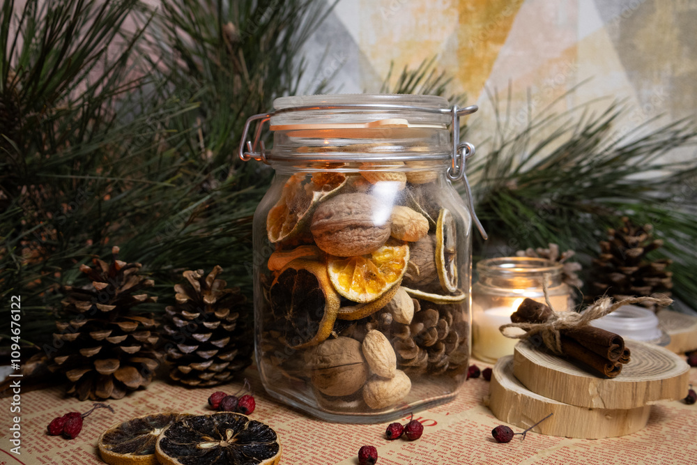Glass jar full with Christmas snacks Nuts dried oranges cinnamon sticks pine cones and branches vanilla candle Glass jar full with Christmas snacks Nuts dried oranges cinnamon sticks pine cones and branches vanilla candle