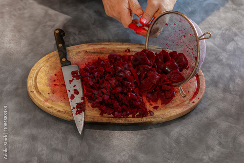 Man Tipping Sliced Beetroot from Strainer onto Oval Wooden Cutting Board with Chopped Beets photo