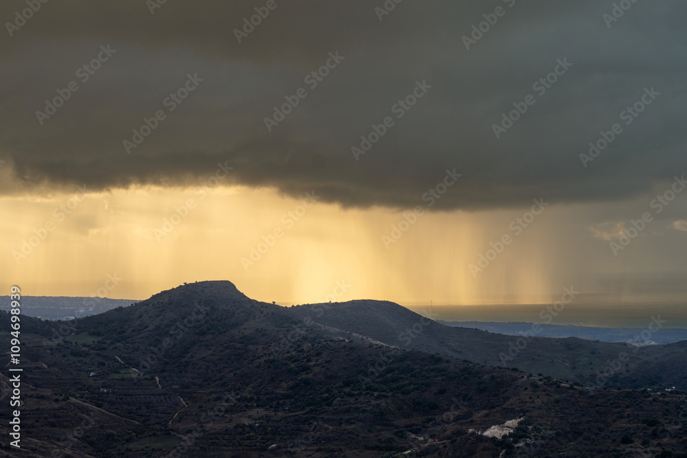 A dramatic landscape featuring heavy rain on a distant sea, illuminated by sunset rays breaking through storm clouds. Scenic view on sea A dramatic landscape featuring heavy rain on a distant sea, illuminated by sunset rays breaking through storm clouds. Scenic view on sea