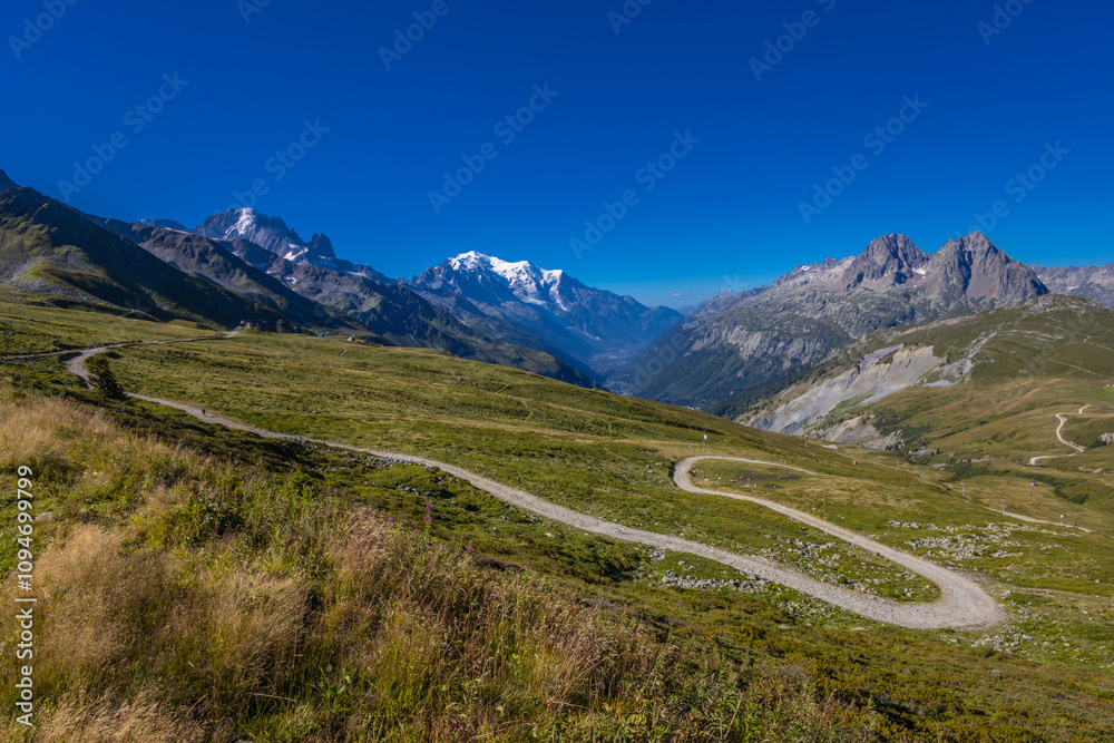 Tour du Mont Blanc beautiful landscapes in the Alps mountains on a sunny summer day. Green grass on the alpine meadow surronded by high mountain peaks of Montbalnc alpine range Tour du Mont Blanc beautiful landscapes in the Alps mountains on a sunny summer day. Green grass on the alpine meadow surronded by high mountain peaks of Montbalnc alpine range