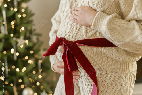 Wallpaper Mural Happy pregnant woman in knitted outfit hugging belly with big red bow close up on background of decorated christmas tree. Pregnancy during holidays, magical joyful time. Best gift Torontodigital.ca