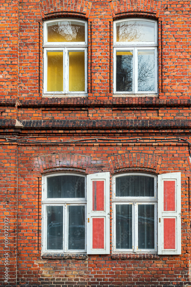 Red brick building with white window frames and open shutters during daylight hours