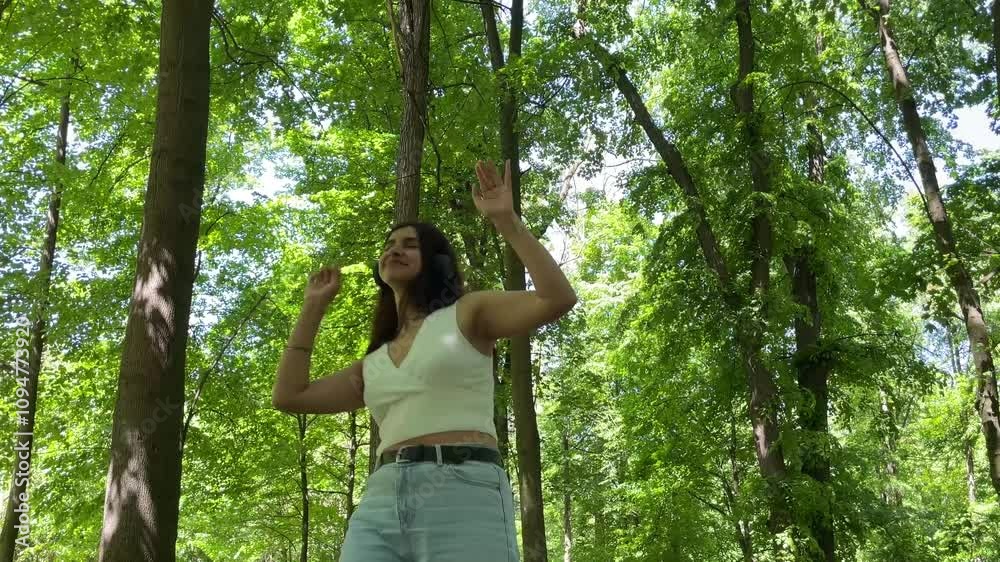Young woman wearing headphones dances joyfully in a sunlit forest, embracing nature and celebrating freedom Young woman wearing headphones dances joyfully in a sunlit forest, embracing nature and celebrating freedom