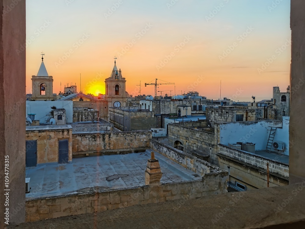 Obraz premium Sunrise over the rooftops and bell towers in Valletta, Malta, casting a warm glow over the historic architecture.