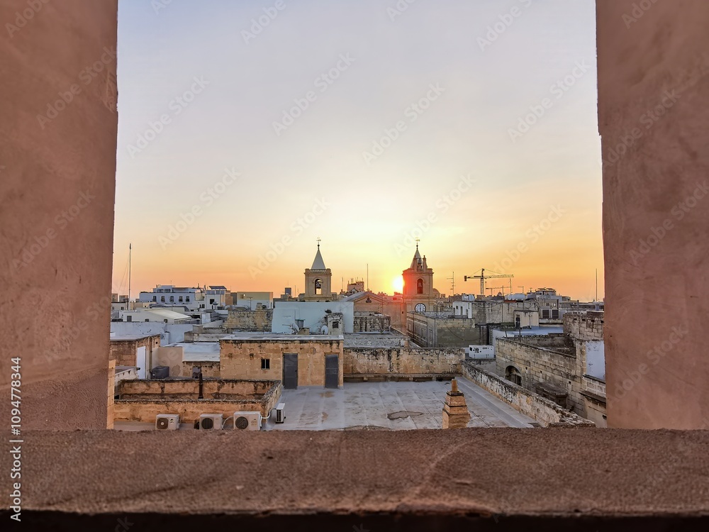 Fototapeta premium Sunrise over Valletta's rooftops, framing historic bell towers and casting a warm glow on the ancient Maltese architecture.