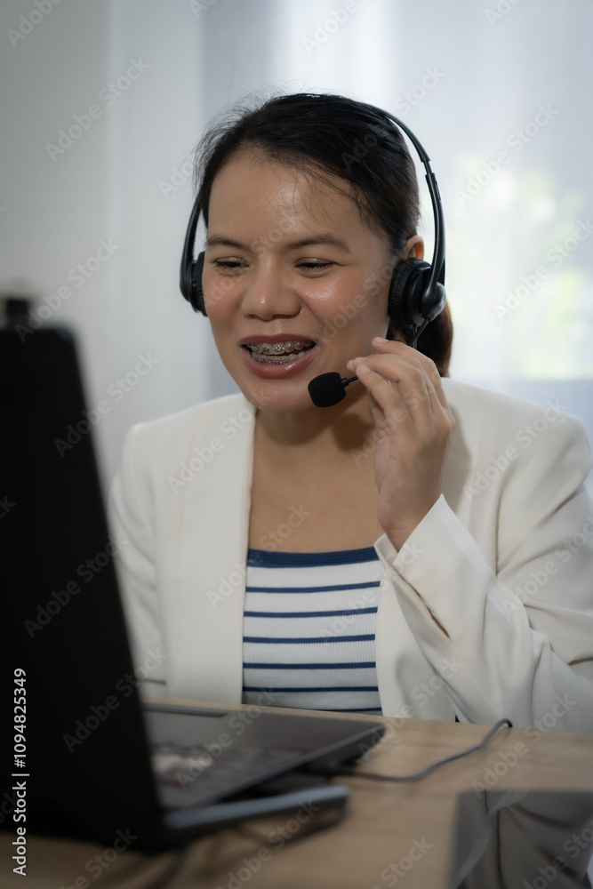 Female operator wearing a white jacket and blue striped shirt is talking on a headset. She is smiling and she is enjoying the conversation Female operator wearing a white jacket and blue striped shirt is talking on a headset. She is smiling and she is enjoying the conversation