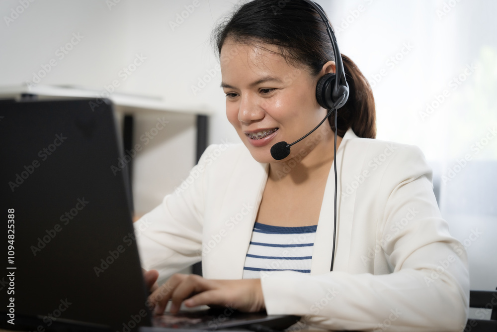 Female operator wearing a headset is typing on a laptop. She is smiling and she is enjoying her work Female operator wearing a headset is typing on a laptop. She is smiling and she is enjoying her work