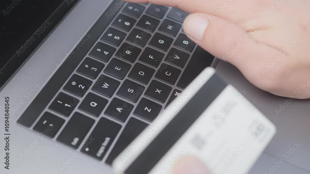 Close-up of a hand holding a credit card, entering information on a laptop keyboard, illustrating online shopping and e-commerce security. Represents modern technology and digital transactions. Close-up of a hand holding a credit card, entering information on a laptop keyboard, illustrating online shopping and e-commerce security. Represents modern technology and digital transactions.