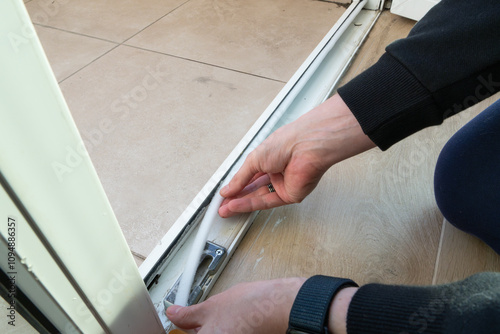 Preparing for the cold season. A man sticks a white foam rubber sealing tape on a door window indoors. Saving Energy Insulating Home Putting Draught Excluder Tape On Window