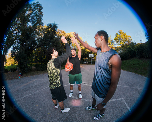 Basketball teammates celebrate with a high five after a successful play on an outdoor court, surrounded by greenery and illuminated by soft sunlight, showcasing teamwork and enthusiasm. photo