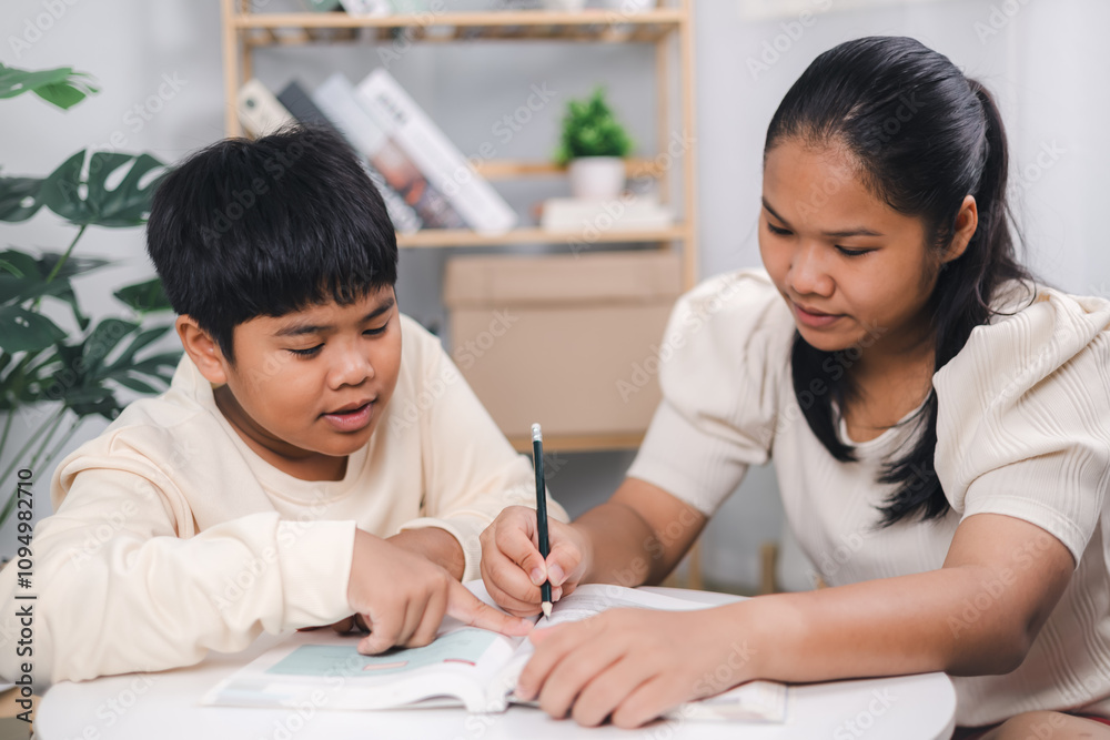 Teacher or sister helping boy writing lesson and learning to write; Female tutor helping little elementary school boy with homework during individual lesson at home; Education home school concept. Teacher or sister helping boy writing lesson and learning to write; Female tutor helping little elementary school boy with homework during individual lesson at home; Education home school concept.