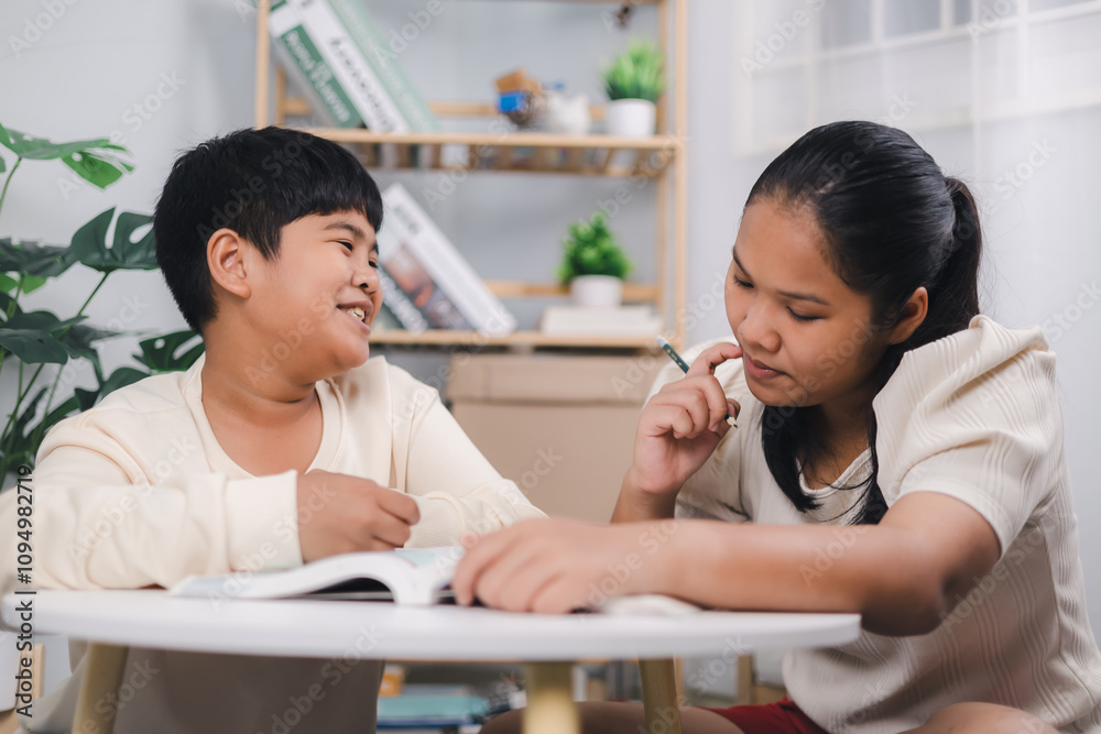 Teacher or sister helping boy writing lesson and learning to write; Female tutor helping little elementary school boy with homework during individual lesson at home; Education home school concept. Teacher or sister helping boy writing lesson and learning to write; Female tutor helping little elementary school boy with homework during individual lesson at home; Education home school concept.