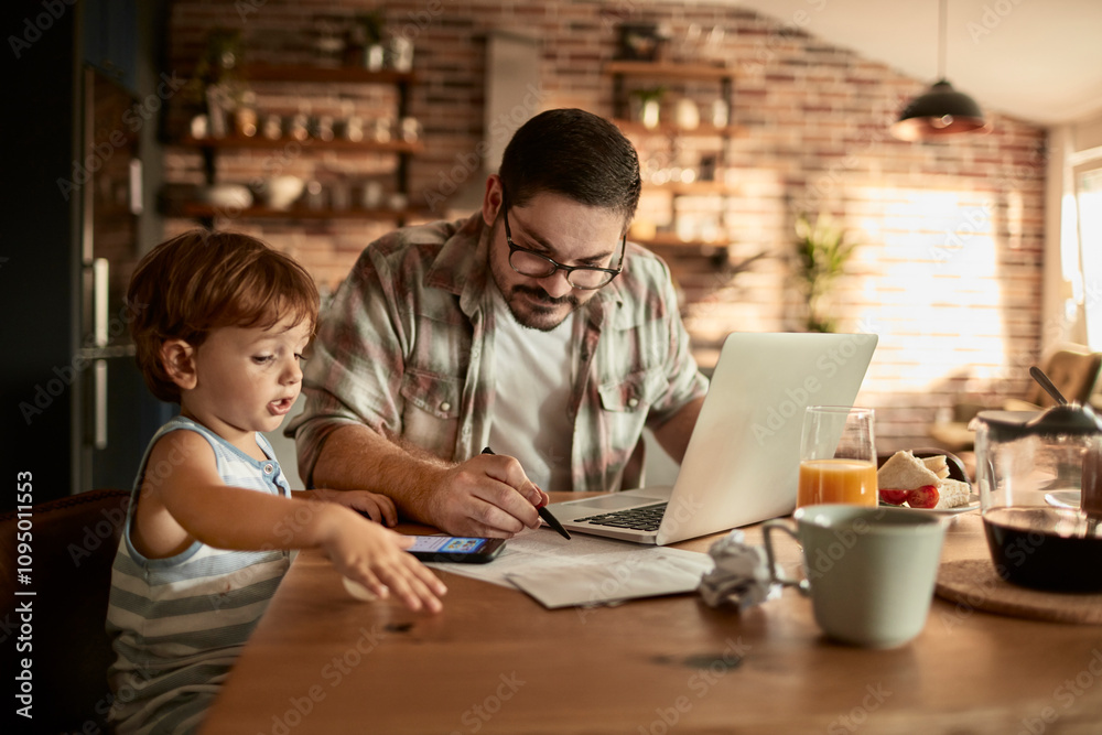 Father working on laptop at home while toddler plays with smartphone Father working on laptop at home while toddler plays with smartphone
