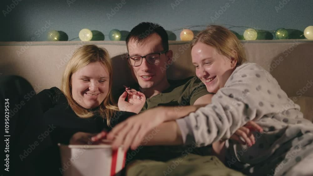 Cheerful young people watching a movie at home, playfully fighting over a handful of popcorn, enjoying time together. Cheerful young people watching a movie at home, playfully fighting over a handful of popcorn, enjoying time together.