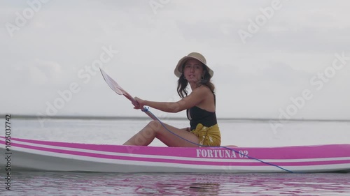 A young female is depicted on the beach, her attention focused intently upon the activity of surfing, which she is undertaking with a view to recreation.