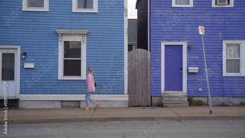 A blond Hair Girl in a Pink Shirt Passing Walking on the Street and Passes by two Blue Houses 4K 