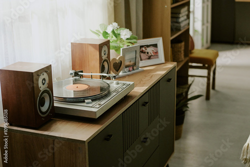 Turntable set on wooden cabinet beside photo frames and potted plants with sunlight streaming through a nearby window, creating a serene and nostalgic ambiance photo