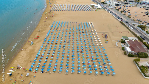 Aerial view of a beach club on a large and crowded sandy beach. There are many people on vacation under the umbrellas. This is the waterfront of Vieste, in province of Foggia, Puglia, Italy. photo