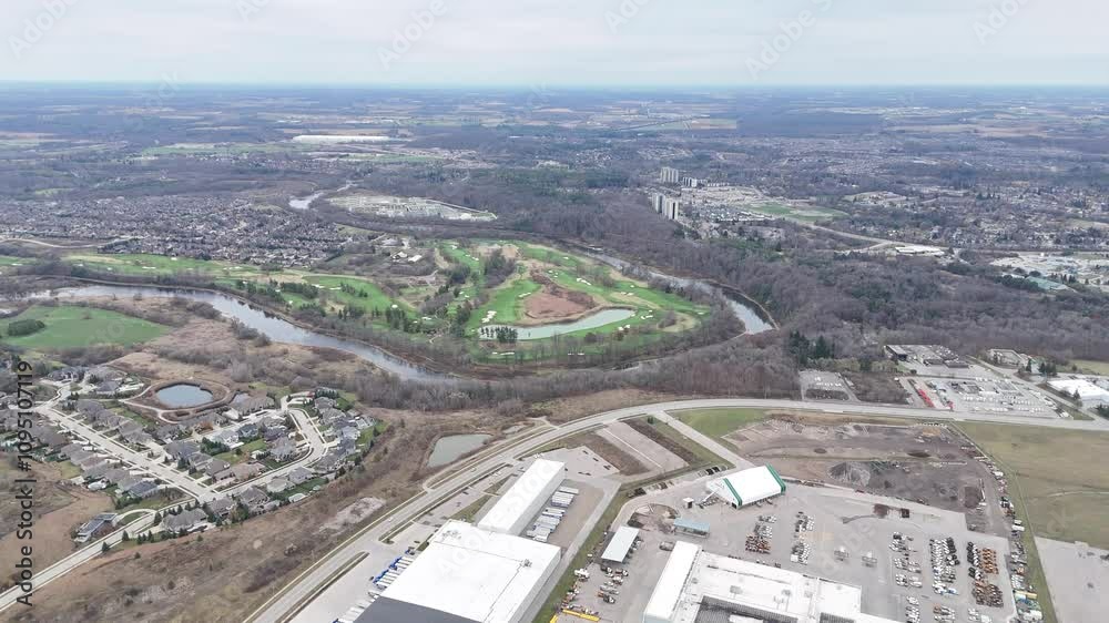 Drone flying over buildings towards a river surrounding a green area with pond in Kitchener Drone flying over buildings towards a river surrounding a green area with pond in Kitchener