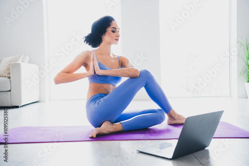 Young woman practicing yoga at home on a purple mat, wearing blue sportswear. She enjoys a healthy lifestyle, focusing on mindfulness.