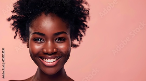 A joyful portrait of a smiling woman with natural hair against a soft pink background.