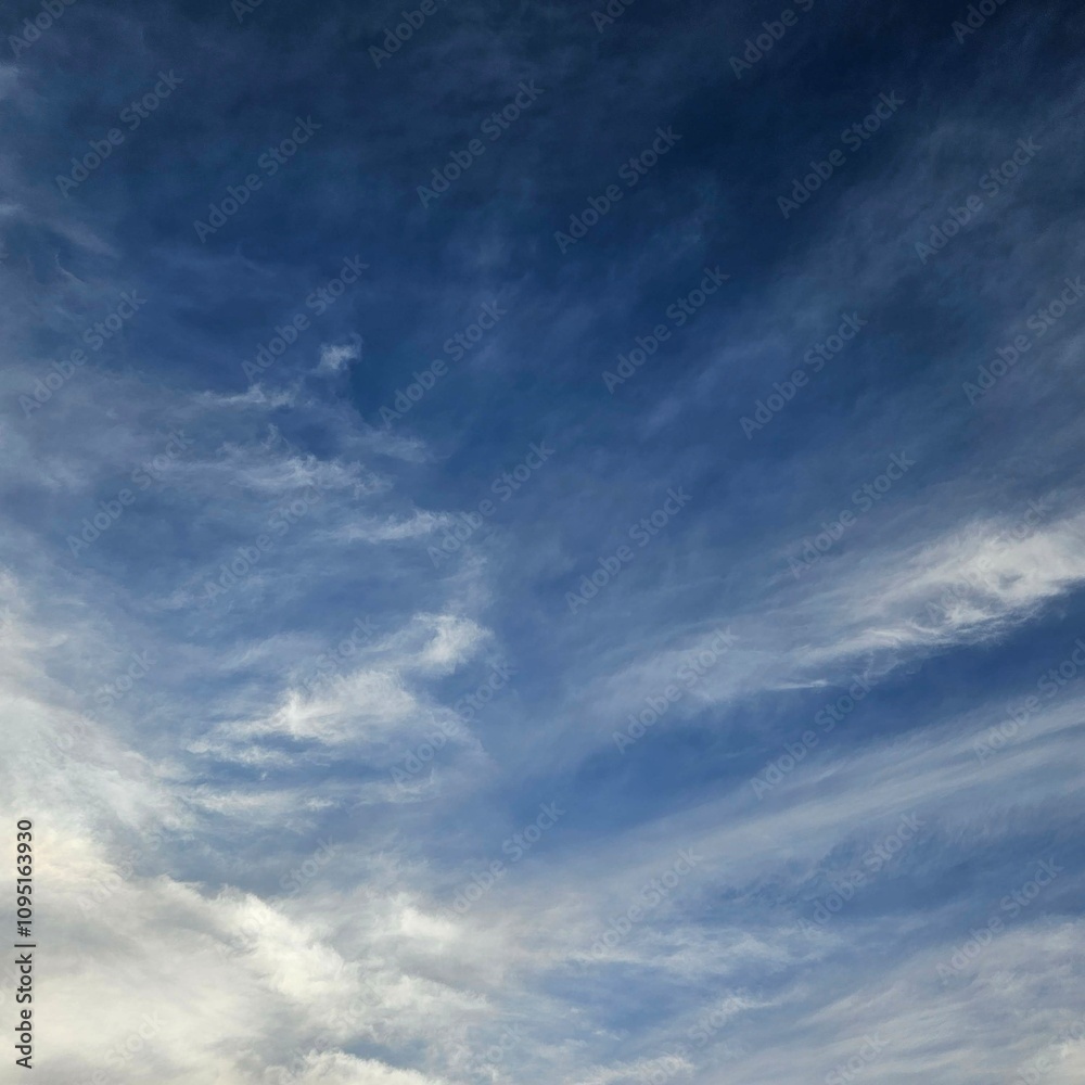 Fototapeta premium Expansive blue sky dotted with wispy white clouds.