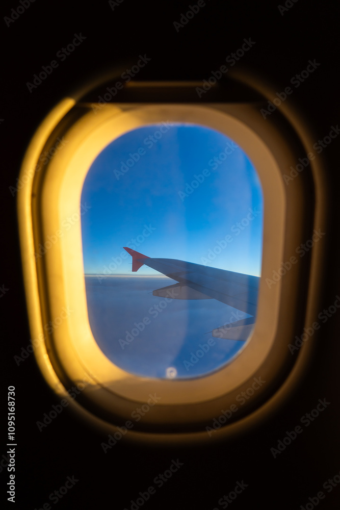 View of aircraft wing against a clear blue sky seen from a passenger window during daytime flight View of aircraft wing against a clear blue sky seen from a passenger window during daytime flight