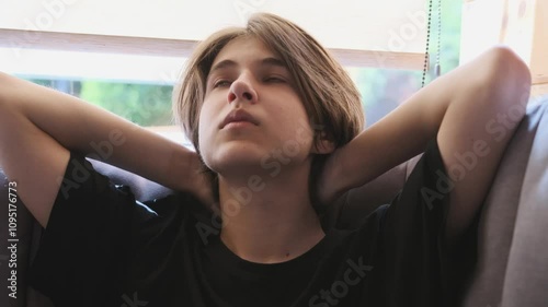 Young man relaxing on a sofa, hands behind his head, enjoying a moment of calm and tranquility in slow motion