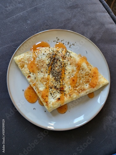 A savory omelette, crispy on the outside and soft on the inside, topped with a drizzle of chili sauce. The omelette is served on a white plate and looks perfect for a quick and easy meal.
