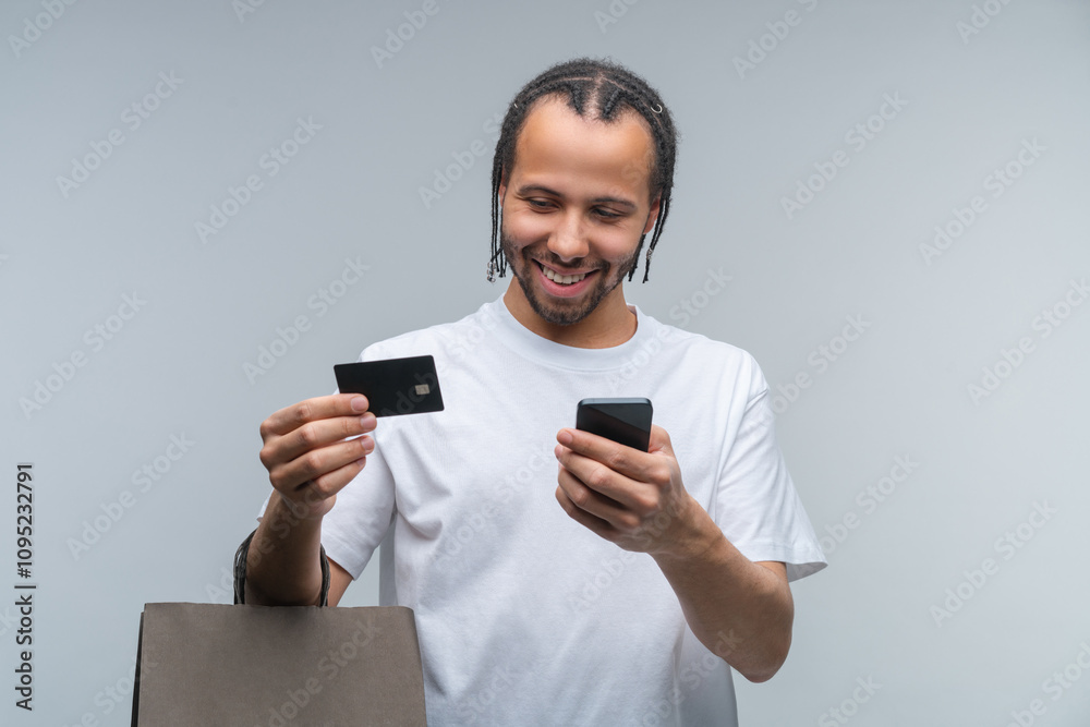 Studio portrait of handsome smiling African American young man making order online via mobile phone using his credit card Studio portrait of handsome smiling African American young man making order online via mobile phone using his credit card