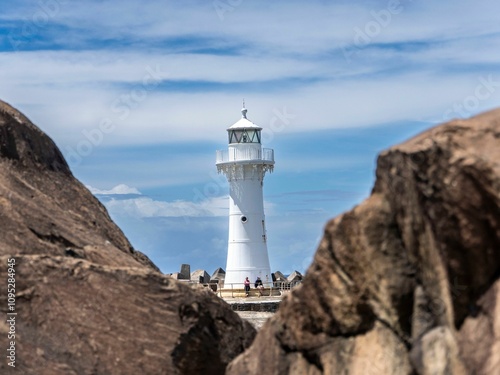 Lighthouse framed by rocks under a blue sky with a couple walking nearby in Wollongong Harbour